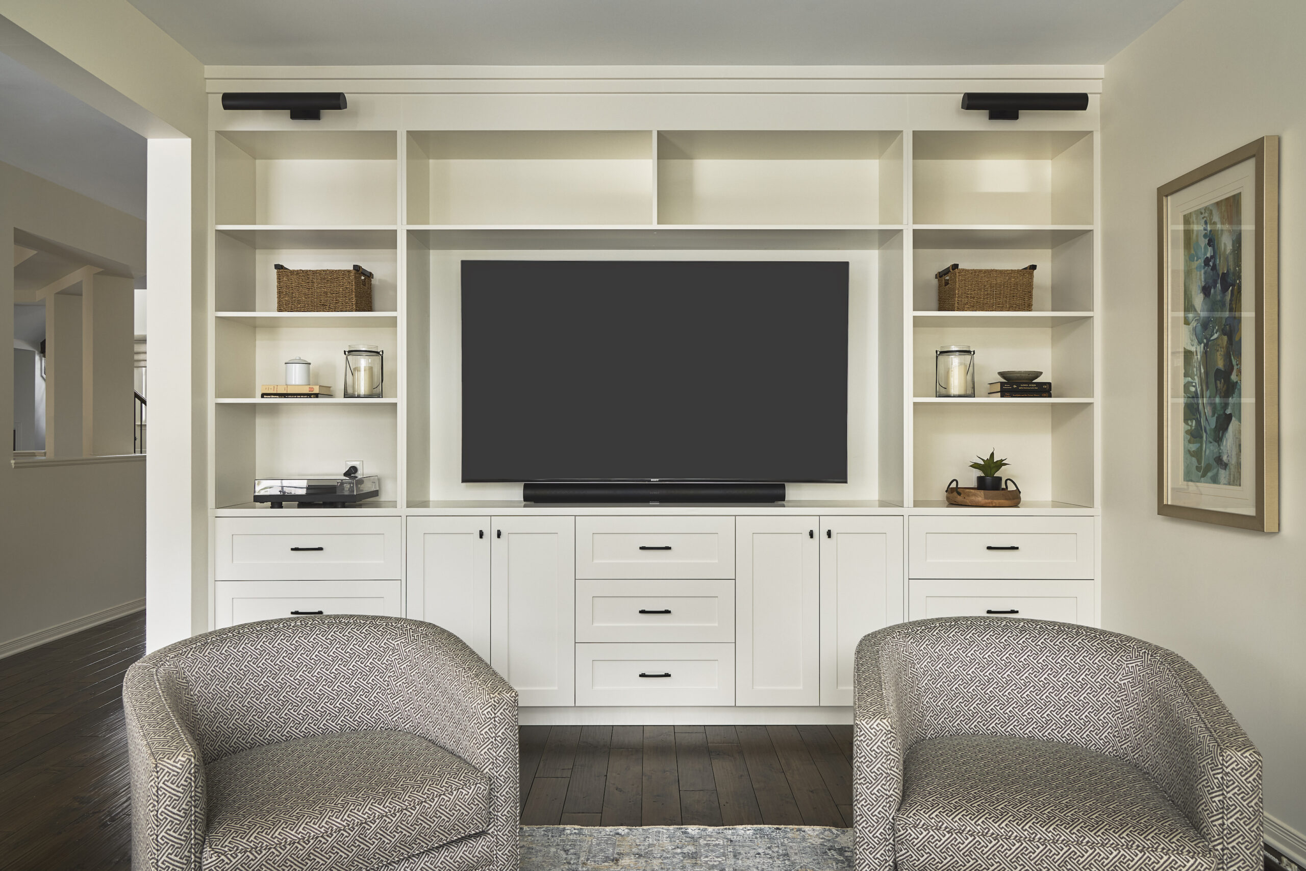 Crisp white custom cabinets serve as an entertainment unit. There are open shelves for memorabilia and closed cabinets and drawers on the bottom to store tv remotes and game consoles.